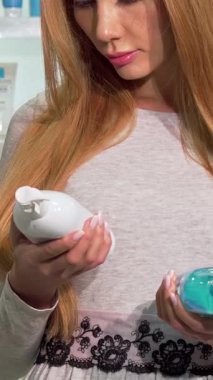 Uzun, dalgalı saçlı düşünceli bir kadın iki şampuan şişesini inceliyor, narin parmakları karar vermeye hazır. Güzellik ürünlerinin kaleydoskopu ile çevrelenmiş olan sahne, bir keşif ve kişisel bakım hissi yayıyor.