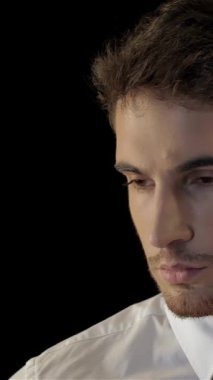 Gıcır gıcır beyaz gömlekli ve parlak siyah kravatlı ciddi bir beyaz adam, çarpıcı bir siyah arka plan karşısında, kulaklığından dikkatle dinliyor. Onun yoğun bakışları ve ince vücut dili özgüven ve uyanıklık yayıyor, özünü somutlaştırıyor.