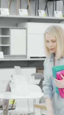 Dalgalı sarı saçlı şık bir kadın modern mobilyalarla dolu şık bir mobilya mağazasında gezinirken canlı havluları dikkatle inceliyor. Anlayışlı bakışları ve düşünceli tavırları ev dekorasyonuna olan tutkusunu yansıtıyor.