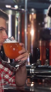 Ekose gömlekli yakışıklı genç bir adam barda oturmuş, dalgınlık, rahatlama ve memnuniyet içinde kaybolurken köpüklü bira içiyor. Barların sıcacık parıltısı ahşap tezgahı parlatıyor ve müşterilerin davetkar konuşmaları samimi bir ortam yaratıyor.