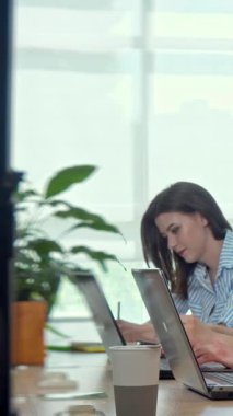 Kendini işine adamış, şık çizgili bir gömlek giymiş genç bir kadın, yeşil ve doğal ışıkla çevrili, gösterişli bir masada işine derinden bağlıdır. Görevlerini yaparken konsantrasyonu ve profesyonelliği ışıldıyor.