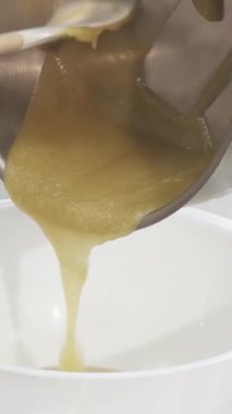 Yetenekli bir pasta şefi zarif bir şekilde pırıl pırıl paslanmaz çelik bir tavadan lekesiz beyaz bir kaseye tatlı yaratma sanatını somutlaştıran ipeksi sıcak krema döker. Bu yakın çekim kremin pürüzsüz, dalgalı dokusunu yakalar ve aşçıya vurgu yapar.