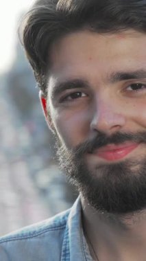 Şık sakallı şık bir genç adam, canlı bir şehir caddesine kurulmuş enerjik bir gülümseme sergiliyor. Rahat duruşu ve kendine güveni pozitifliğini gözler önüne seriyor, dinamik kentsel yaşam tarzını benimsiyor.