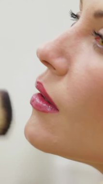 Göz kamaştırıcı bir kadın şık bir kuaförün ışıltısında güneşleniyor, büyüleyici bir makyajdan geçiyor yetenekli bir güzellik uzmanı nazikçe yumuşak bir fırçayla makyaj yapıyor. Hava heyecan ve zarafetle dolu. Dönüşümü vurguluyor.