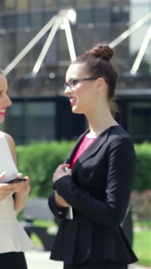 Hareketli bir şehir manzarasında, kendine güvenen genç bir iş kadını, parlak tabletinden haberleri dikkatle okur, profesyonellik yayar. Yakınlarda, şık meslektaşları, işbirliğiyle dolu enerjik bir atmosfer yaratarak, canlı bir konuşma yapıyorlar.