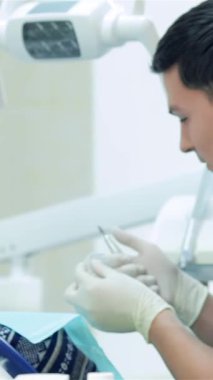 Neşeli bir dişçi asistanı, temiz bir klinikte dişçi aletlerini titizlikle hazırlayan odaklanmış bir dişçinin yanında otururken parlak bir gülümsemeyle pozitiflik yayar. Bu canlı sahne takım çalışmasının sinerjisini güzel bir şekilde gösteriyor.