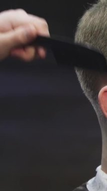 Bu yakın çekim, yetenekli bir berberin saçını elektrikli makasla titizlikle budarken kendine güveni yayan yakışıklı bir delikanlıyı gösteriyor. Şık berber dükkanı atmosferi enerjiyle uğulduyor, modern tımarcılığın sanatsallığını ve hassasiyetini vurguluyor.