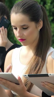 Üç dinamik iş kadını şık resmi giysiler içinde tabletlerine daldırılırken, biri telefonuna güvenle konuşarak canlı bir şirket atmosferini somutlaştırıyor. Odaklanmış ifadeleri ve şık kıyafetleri profesyonellik saçıyor.