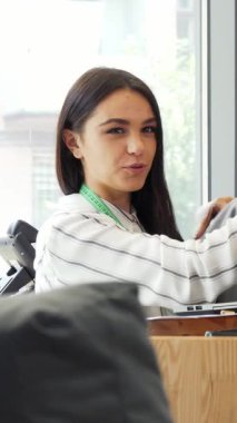 Uzun siyah saçlı ve parlak gülüşlü, ışıl ışıl genç bir bayan tasarımcı, güneşli modern bir ofiste meslektaşı ile tutkuyla bir tişört tasarımını tartışıyor. Titreşimli atmosfer yaratıcılığı ve takım çalışmasını yansıtıyor.