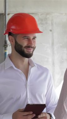 Gıcır gıcır beyaz gömlekli ve parlak turuncu şapkalı genç, sakallı bir inşaat mühendisi, canlı bir inşaat alanındaki takım çalışmasının ruhunu somutlaştıran bir meslektaşla canlı bir tartışmaya girişiyor. İnceleme sırasında hava enerjiyle doludur.