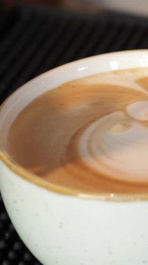 Yetenekli bir erkek barista, sıcaklığı yayıyor, kadife sütü titizlikle döküyor, canlı bir kahve tezgahında kremalı kapuçino üzerine çarpıcı bir latte sanatı yaratmak için. Davetkar atmosfer, taze demlenmiş espresso ve nazik espressonun zengin aromasıyla zenginleşir.