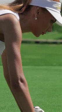 Büyüleyici bir yan bakış, dört ayak üzerinde duran kızıl saçlı çarpıcı bir golfçüyü yakalıyor ve vurmaya hazırlanırken deliğe odaklanıyor. Pürüzsüz beyaz bir etek ve üzerine de bir tişört giymiş olan bu beyaz atletik kadın güneş ışığıyla yaz titreşimleri yayıyor.