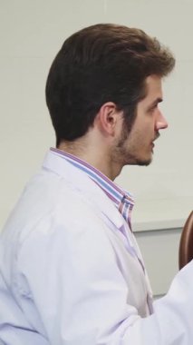 Parlak, steril bir klinikte, yetenekli bir dişçi dişçi dişlerinin kalıbını olgun erkek hastasına tutkuyla açıklar, o da rahat bir diş hekimi koltuğunda oturur. Bu dinamik etkileşim hasta eğitiminin dişçilikteki hayati rolünü vurgular.