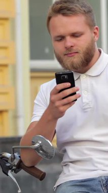 Şık, bakımlı sakallı genç bir adam scooter 'ında dinleniyor, akıllı telefonuna dalmış. Canlı kentsel ortam renklerle dolup taşıyor, tasasız yaz maceralarının özünü yakalıyor ve modern boş zamanların neşesini yakalıyor.