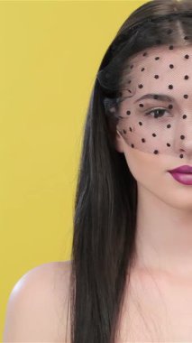 Uzun, esmer saçlı, büyüleyici bir Asyalı kadın zarif bir şekilde zarif bir siyah peçeyle çerçevelenmiş avucunun içine bakar. Parlak sarı bir zemin üzerine kurulmuş bu çarpıcı görüntü karmaşıklık ve cazibe yayıyor.