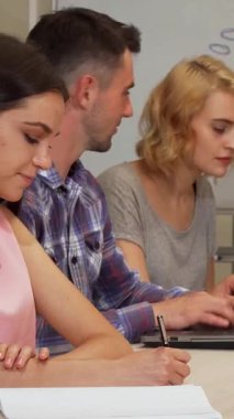 Neşeli bir kız öğrenci kameraya ışıldıyor, çalışmalarına dalmış arkadaşlarıyla işbirliği yaparken coşkulu gülümsemesi odayı aydınlatıyor. Bu dinamik sahne, takım çalışmasının enerjisini ve öğrenmenin heyecanını yansıtıyor.