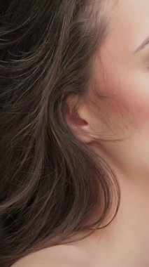 Bu büyüleyici, yavaş çekim sahnesinde, dalgalı esmer saçlı, çarpıcı beyaz bir kadın çarpıcı bir siyah arka planda parlayan kusursuz cildiyle büyülüyor. Işıl ışıl güzelliğinin ve kıvrımlı dumanın yan yana gelişi.