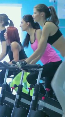 Dört enerjik kız arkadaş, parlak ve modern bir spor salonunda, spor ve sağlığa olan sarsılmaz bağlılıklarını göstermek için, parlak, durgun bisikletlerin üzerinde tutkuyla pedal çeviriyorlar. Canlı atmosfer, canlı mavi duvarlar ve akan doğal ışık ile vurgulanır.
