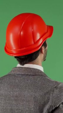 Gösterişli bir takım elbise ve parlak turuncu kasketli bir erkek mühendisin dikiz görüntüsü, canlı yeşil renkli bir ekrana bakarken hayal kırıklığı içinde boynunu ovuyor. Bu çarpıcı görüntü, yapıdaki hayal kırıklığının ve stresin ağırlığını özetliyor.