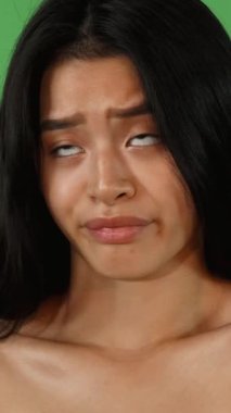 Uzun, dalgalı saçları olan çarpıcı bir Asyalı genç kadın canlı yeşil renkli bir arka plana karşı poz veriyor. Şüpheci ifadesi hayal kırıklığı yayıyor. Kusursuz cildi ve etkileyici özellikleri duygusal bir derinlik yakalıyor.