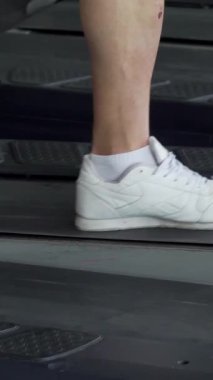 Kolsuz gömlekli kararlı bir adam koşu bandında rahatça yürür. Antrenmanını akıllı telefon ile dengede tutar. Bu dinamik sahne, modern fitness 'in özünü yakalıyor. Teknoloji, canlı bir spor salonunda adanmışlıkla buluşuyor.