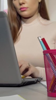 Kesilmiş bir atış, çalışmalarını yaparken parlak pembe bir bardak tutacağından kalem almaya çalışan kararlı bir üniversite öğrencisini yakalar. Notlar ve dizüstü bilgisayarla çevrili halde akademik başarı ve yaratıcılık ruhunu somutlaştırıyor.