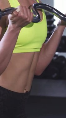 Odaklanmış bir sporcu kadın, modern bir spor salonunda kaslı vücudunu ve kaslarını ustalıkla biceps kıvrımlarını bir ez kıvrım çubuğuyla sergiliyor. Bu dinamik sahne gücün ve adanmışlığın özünü somutlaştırıyor.