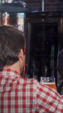 Sıcak bir gülümsemesi olan çekici bir barmen hayat dolu bir barda iki memnun müşteriye ferahlatıcı el yapımı bira doldurur. Kahkaha ve arkadaşlıkla dolu davetkar atmosfer hafta sonu rahatlığının ve sosyal zevkin özünü yakalıyor.