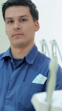 Mavi üniformalı neşeli bir erkek dişçi modern bir diş muayenehanesinde gülümserken başparmak kaldırıyor. Sıcak tavırları ve iyi donanımlı çevresi birinci sınıf diş bakımı isteyen hastalar için hoş karşılayıcı bir ortam yaratıyor.