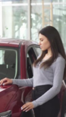 Neşeli genç bir kadın heyecanla ışıldıyor, bir elinde araba anahtarlarını gösteriyor ve yeni arabasının önünde başparmağını kaldırıyor. Satıcının canlı atmosferi, onun mutluluğunu ve başarı duygusunu vurguluyor.