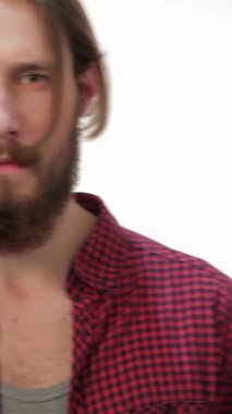 Çekici, bakımlı sakallı ve uzun saçlı genç bir hippi çağdaş stüdyo ortamında rahatça poz veriyor. Ekose gömleği ve ciddi ifadesi havalı, modern bir hava yayıyor. Yaşam tarzı ve moda teması için mükemmel.