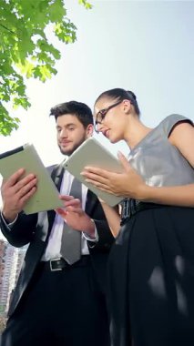 Kendine güvenen bir işadamı ve başarılı bir iş kadını, modern mimariyle çevrili kentsel bir ortamda tabletleri kullanırken canlı bir tartışmaya girişirler. Gülüşleri işbirliğinin ve başarının sevincini yansıtıyor.