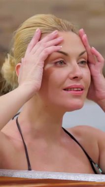 Işıl ışıl sarı saçları olan mutlu genç bir kadın köpüren bir jakuzide sakin bir şekilde ıslanmaktan zevk alıyor. Gülüşü sakin atmosferi aydınlatıyor. Rahatlatıcı su jetleri ve lüks bir kaplıca arkaplanı ile çevrili, rahatlamanın özünü somutlaştırıyor ve