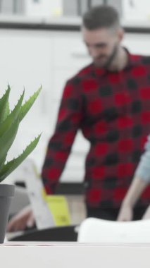 Zevkli bir çift, mutluluk saçan, çağdaş bir mağazada şık mobilya parçalarını hevesle inceliyor, ön planda canlı bir saksı bitkisi ve yeşillik katıyor. Ortak heyecanları ve bağlantıları bir...