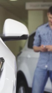 Heyecanlı genç bir çift, parlak, modern bir bayilikte, parlak beyaz bir araba tarafından büyülenmiş, akıllı telefonlarıyla anı yakalıyorlar. Bu canlı sahne neşe saçıyor ve birlikte bir otomotiv macerasına atılmanın heyecanı sergileniyor.