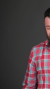 Gösterişli ekose gömlekli şık sakallı bir adam boynunun arkasını tırmalıyor, parlak, koyu gri arka planda derin düşüncelere dalmış. Anlamlı gözleri ve kıvırcık saçları içsel bir bakış açısı, modern erkekliğin somutlaştırılması ve...