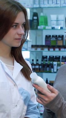 Gıcır gıcır beyaz önlüklü neşeli bir eczacı ve arkadaş canlısı bir bayan müşteri canlı bir eczanede cilt bakımı yapan bir ürünü keşfederken çok ilgi çekici bir anı paylaşıyorlar. Sağlıklı ve güzel eşyalarla dolu renkli raflar davetkar bir davet yaratıyor.