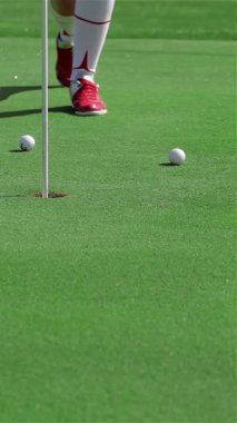 Kararlı genç bir Kafkasyalı kadın, golf topuna sarsılmaz bir hassasiyetle vurmaya hazırlanan canlı zümrüt çimlerin üzerinde zarafetle diz çöker. Şık kırmızı ayakkabıları yemyeşil arka planda patlıyor. Spor ve hırs ruhunu somutlaştırıyor.