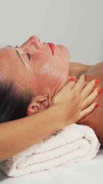 Mutlu, olgun bir kadın, yetenekli bir terapistin, sakin bir spa atmosferiyle çevrili boynuna ve omuzlarına nazikçe masaj yaparken rahatlamanın tadını çıkarıyor. Yumuşak, sıcak aydınlatma ve dingin atmosfer gençleşme deneyimini arttırır, derin bir promosyon sağlar.