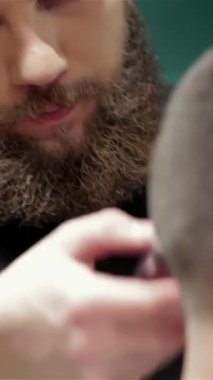 Büyüleyici bir klasik berber dükkanında kendini işine adamış bir berber, sakallı bir adamın saçını ustalıkla tarar ve sanatını sergiler. Sıcak ışıklandırma ve retro dekor, kişisel deneyimlerini vurgulayarak davetkar bir atmosfer yaratıyor.