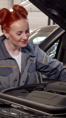 Kızıl saçlı yetenekli ve şık bir bayan tamirci parlak, modern bir garajda şık bir cipin motorunu titizlikle inceliyor. Odaklanmış tavrı ve profesyonel kıyafeti güven yayıyor, kadınların güçlendirici varlığını gösteriyor.