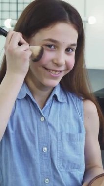 Uzun, dalgalı kahverengi saçlı ışıl ışıl küçük bir kız şık bir salon ortamında allık sürerken zevkten dört köşe oluyor. Neşeli enerjisi ve masum cazibesi, çocukluk neşesinin ve yaratıcılığının özünü yansıtıyor.