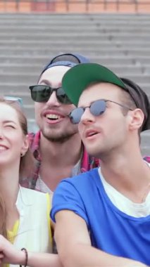 Genç arkadaşlardan oluşan canlı bir üçlü, bir erkek ve iki kadın, açık hava basamaklarında neşeyle selfie çekiyorlar, mutluluk ve dostluk yayıyorlar. Şık kıyafetleri ve ışıl ışıl gülümsemeleri heyecan verici bir atmosfer yaratıyor, ölümsüzleştirmek için mükemmel.