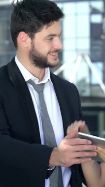 Kendine güvenen bir işadamı ve başarılı bir iş kadını açık havada yaptıkları işbirliğini neşeyle kutluyor, parlak bir tablet üzerinde yenilikçi fikirler alışverişinde bulunuyorlar. Işıl ışıl gülüşleri ve şık iş kıyafetleri canlı bir şehir zeminine karşı parıldıyor.