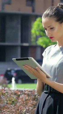 Canlı bir şehir manzarasında, kendine güvenen genç bir iş kadını tabletine sarılıp profesyonellik ve tarz yayıyor. Onun sıcak gülümsemesi, meslektaşlarının yakınlarda etkileşime geçtiği hareketli ve dinamik bir çalışma atmosferini somutlaştıran hareketli sahneyi canlandırıyor.