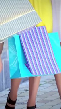 Üç modaya uygun kız, her biri neşeli renklerde canlı alışveriş torbaları taşıyor, şık bir alışveriş bölgesinde gezinirken neşe ve heyecan saçıyorlar. Şık kıyafetleri ve bulaşıcı kahkahaları, canlı bir atmosfer yaratıyor.