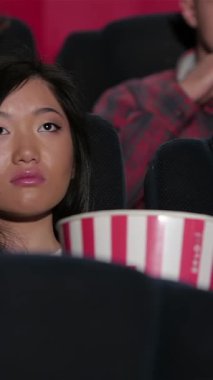 Neşeli bir çift loş, karanlık tiyatro koltuklarında oturur, büyük ekranda titreyen filme dalmış, istekli bir seyirci tarafından çevrelenmiş. Geniş çizgili patlamış mısır kovasını paylaşırken canlı atmosfer heyecanla dolup taşıyor.