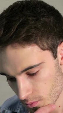 Şık, mavi kotlu genç bir adam şık gri bir tuğla zemine karşı düşünceli bir duruş sergiliyor. Çekici bir gülümseme ve derin bir bakışla, özgüven ve modern bir yetenek yayıyor, hayranlık uyandırıyor.