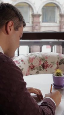 Esmer saçlı genç beyaz bir adam büyüleyici bir kafede kahvenin zengin aromasının tadını çıkarıyor. Not defterine notlar yazmakla çok meşgul. Samimi bir süveter giyerek, açık sayfalara düşünceli bir şekilde sarı bir kalem yerleştirir.