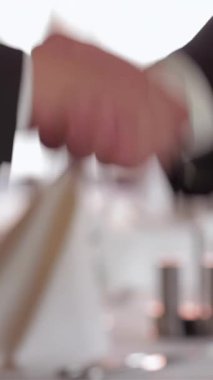 Yumuşak ışıklandırma ve zarif dekor ile süslenmiş şık bir restoranda, iki iyi giyimli iş adamı sıkı bir tokalaşma içinde, umut verici bir ortaklığı sağlamlaştırıyorlar. Sofistike bir ortam, düzgünce düzenlenmiş masalar ve sıcak